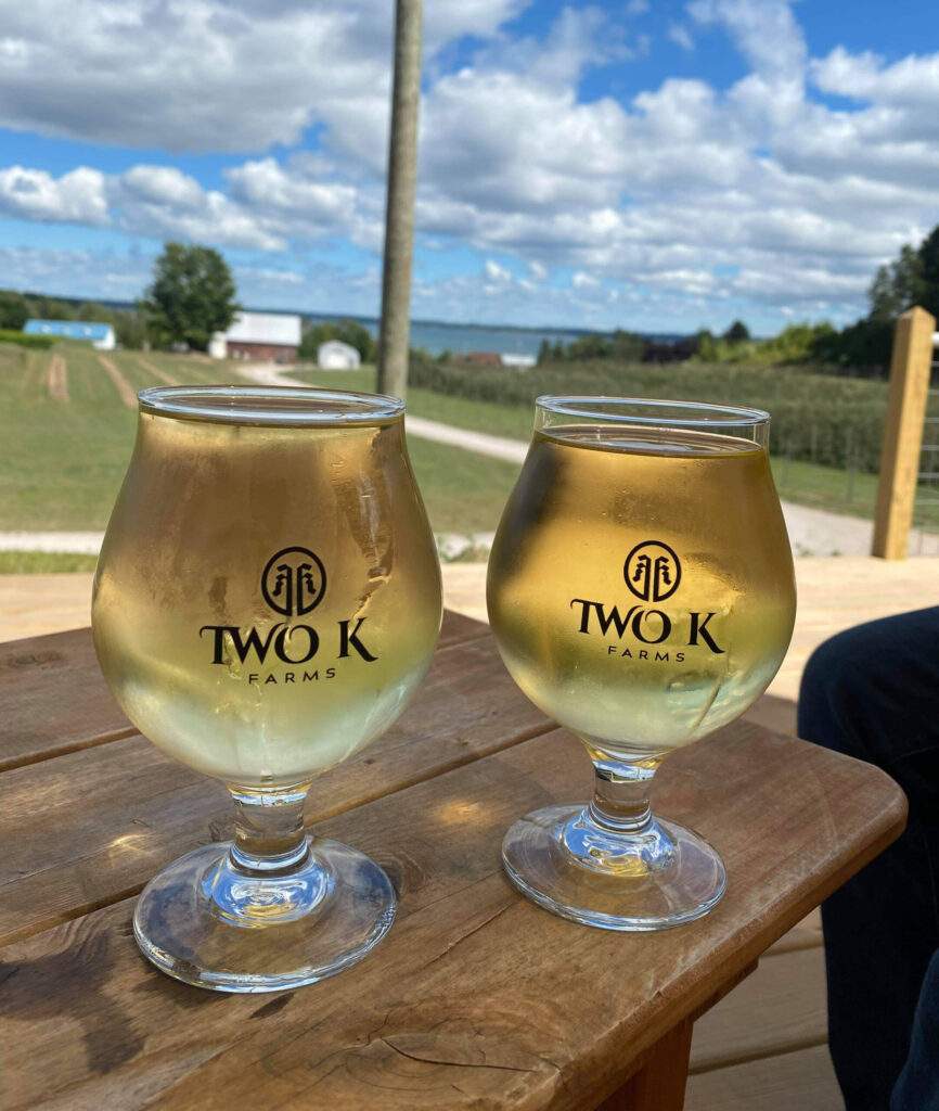 Photo of two Two K farms cider glasses sitting on a wooden table on a sunny day outside the Two K Farms tasting room.
