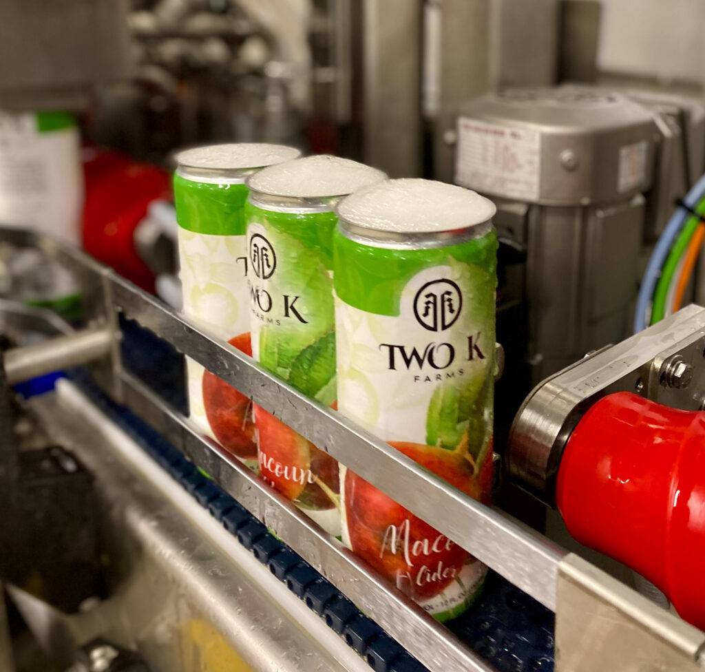 Photo of three cider cans on a conveyer. They have just been filled and are awaiting tops.