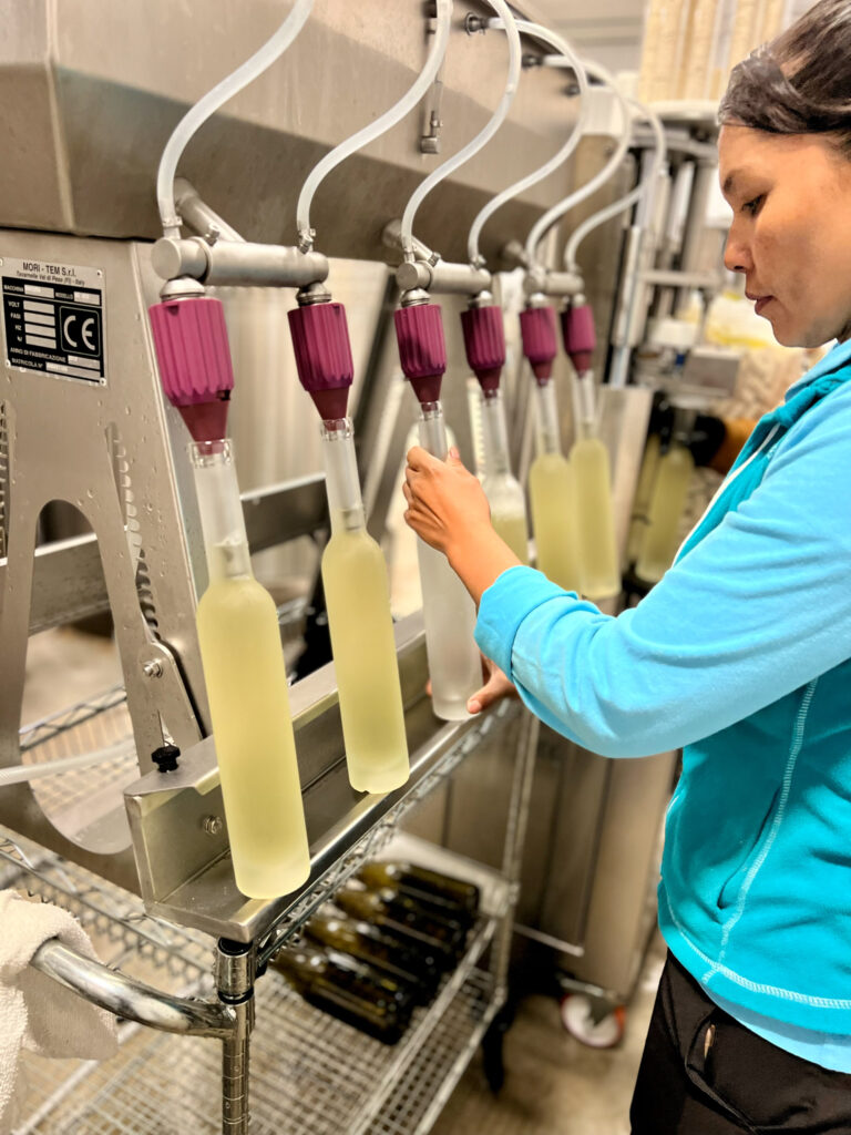 Photo of an employee using bottling equipment to fill frosted glass wine bottles with Ice Cider.