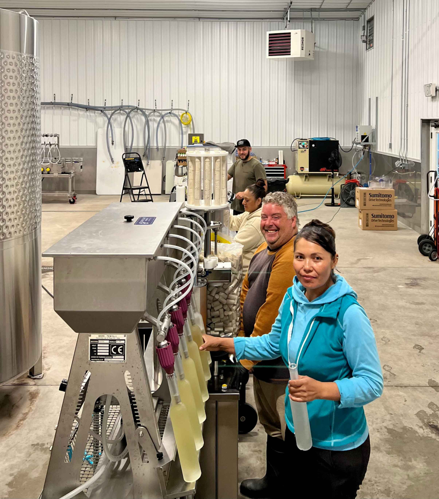 Photo of Two K Farms employees working to fill bottles of Ice Cider using processing equipment.