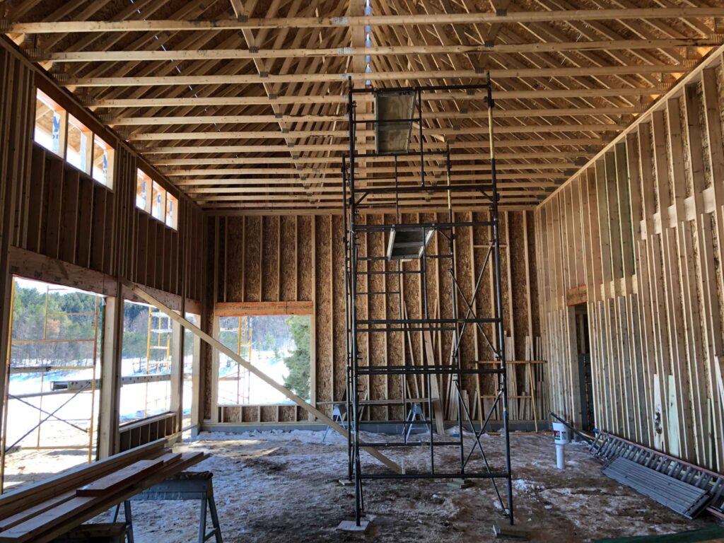 Photo of the inside of a newly constructed wood building with window and door openings. There is a scaffolding in the middle of the building and exposed wooden rafters.