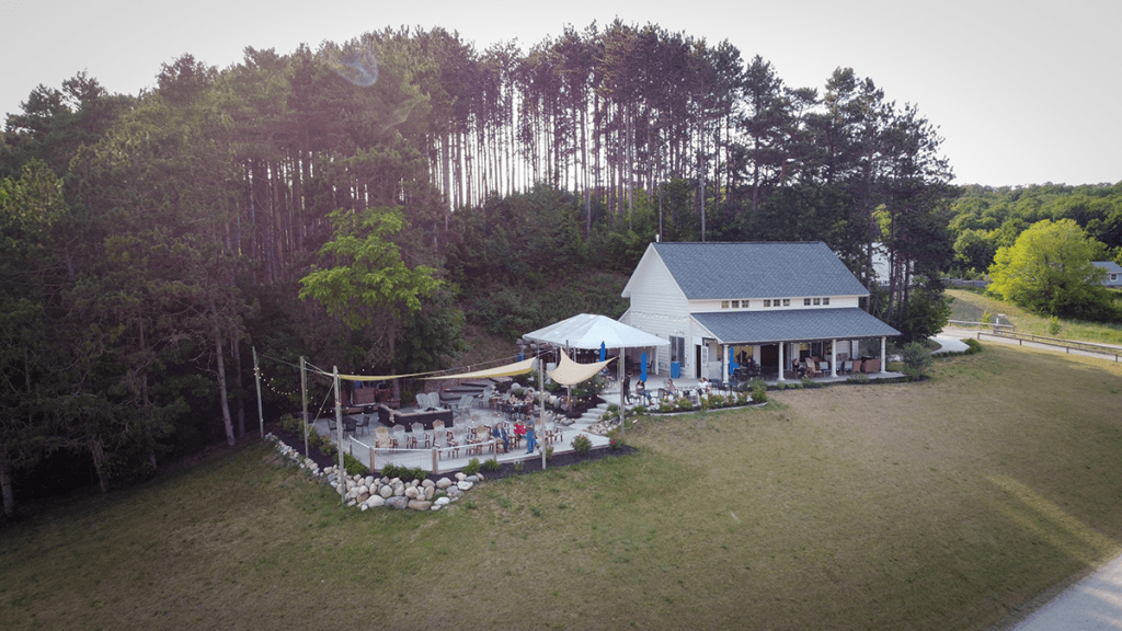 Aerial photo of the Two K Farms tasting room and patio. There is green grass in the foreground and a small pine tree forest behind the tasting room.